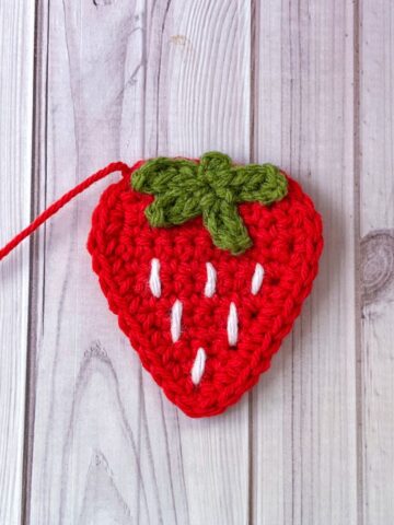 Finished crochet strawberry applique on a wooden table.