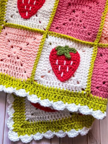 Finished crochet strawberry blanket on a wooden table.