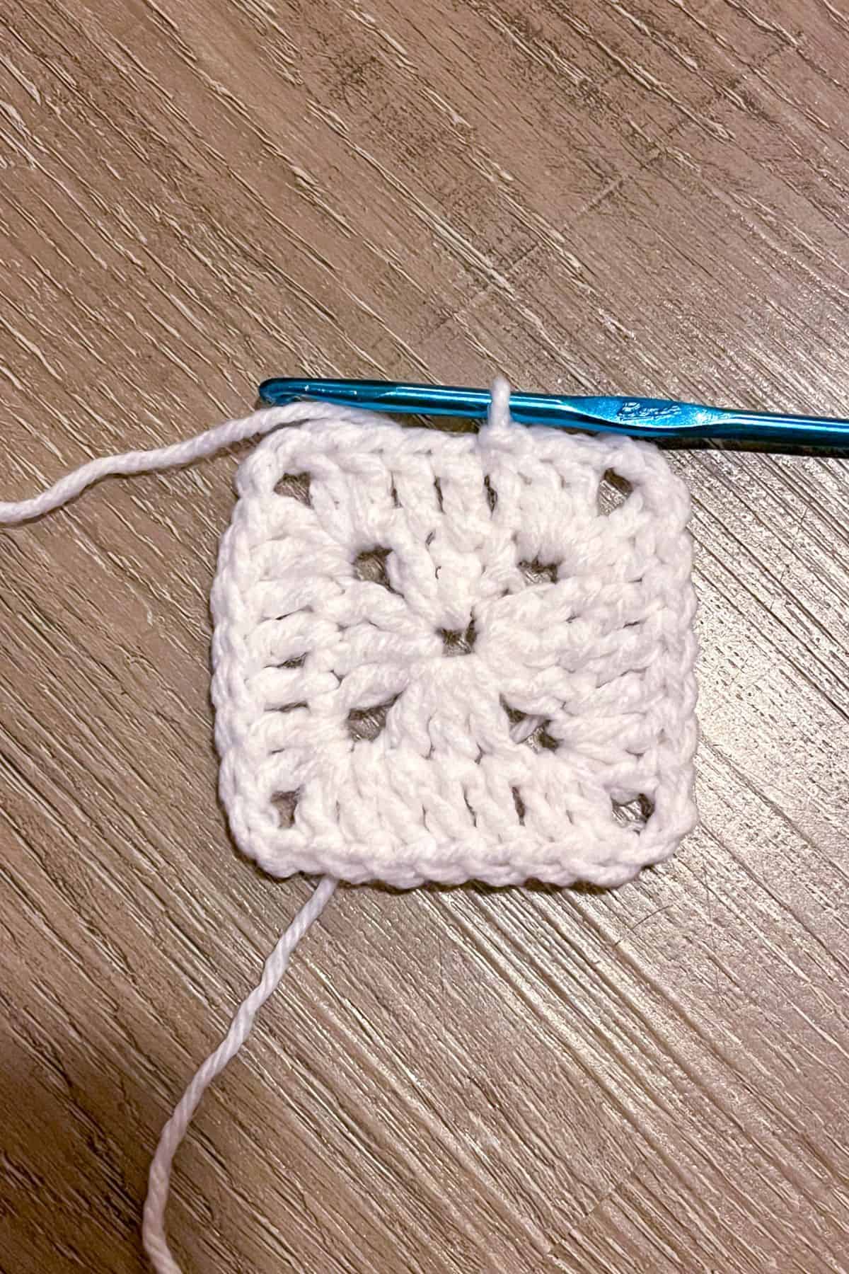 The second round of a crochet granny square using white yarn.