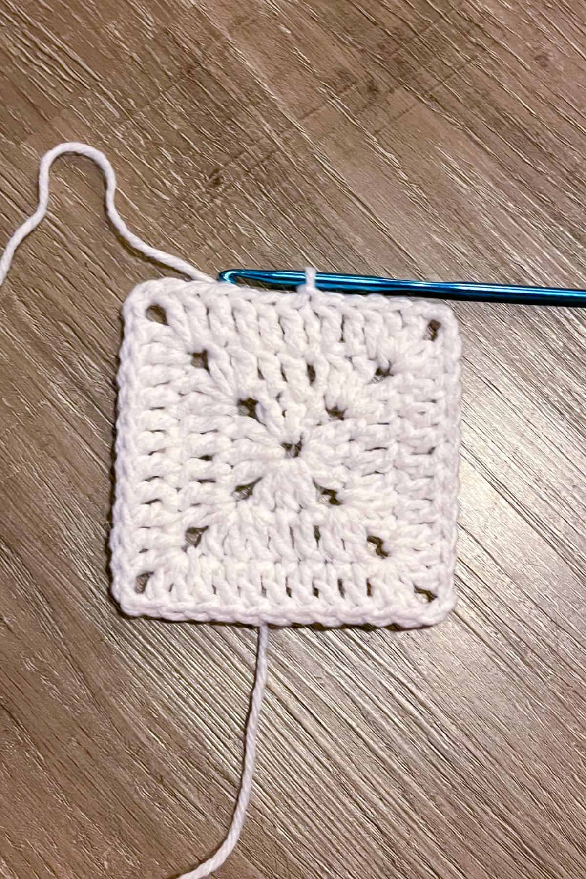 The third round of a solid crochet granny square using white yarn.