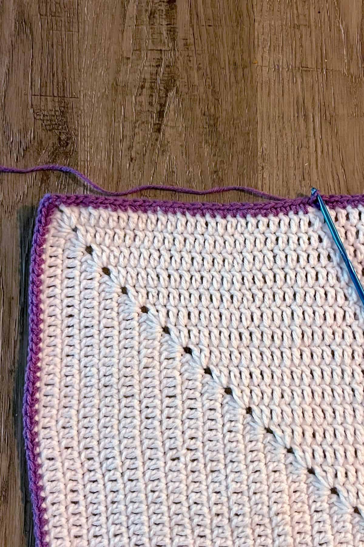 Single crochet purple round around the white solid granny square.
