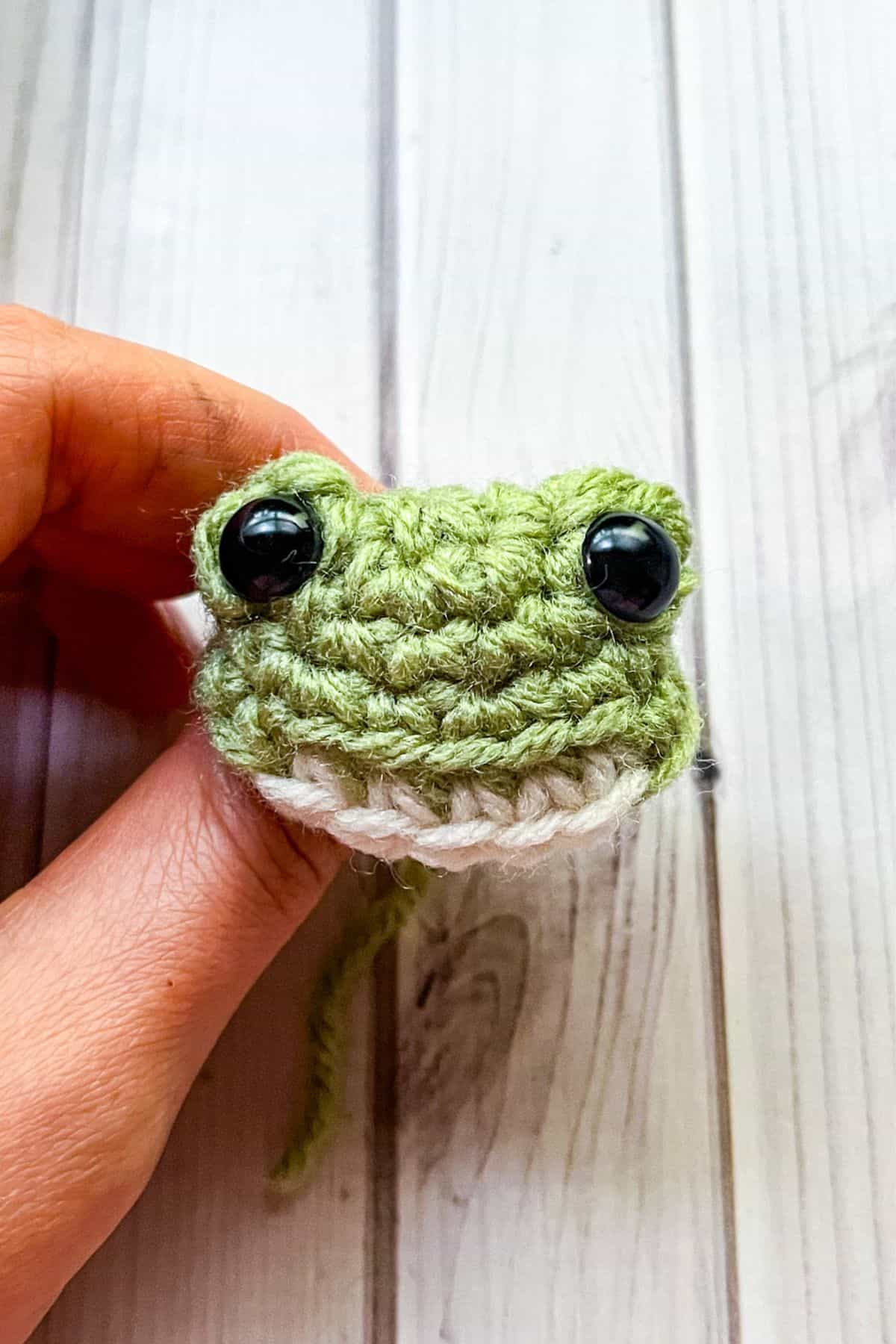 Adding safety eyes to the crochet frog face.