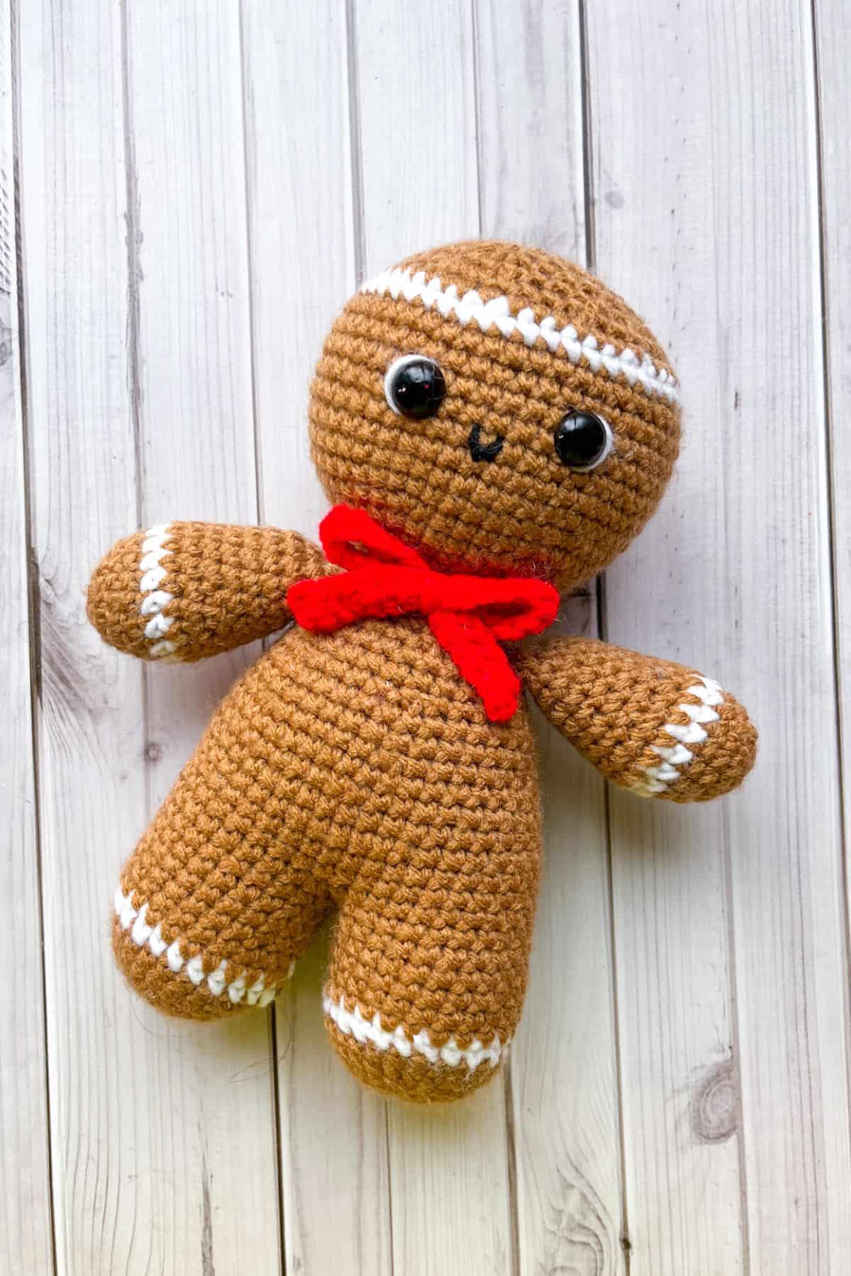 Crochet gingerbread man plush toy with black button eyes and red bow.