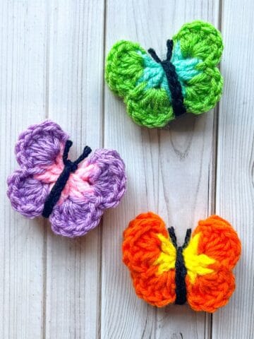 3 crochet butterfly appliques on a table.