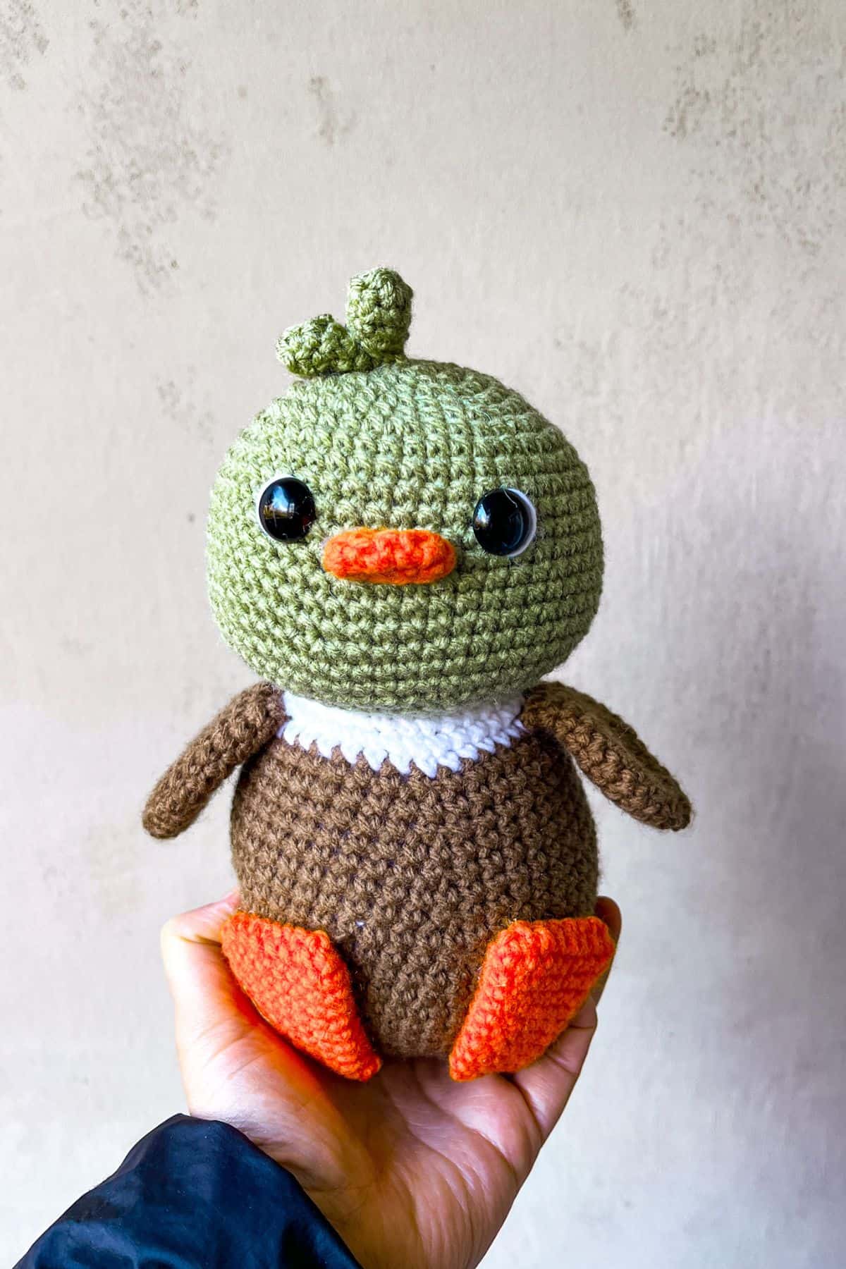 Crochet mallard duck is being held up to a plain background.