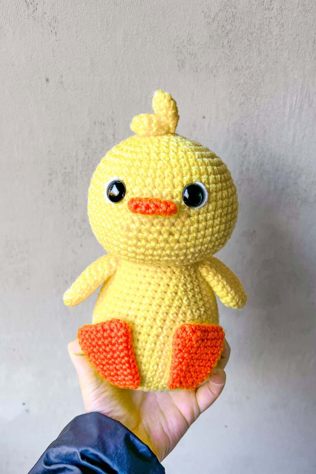 Crochet yellow duck is being held up to a plain background.