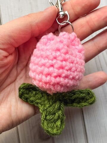 Crochet tulip keychain in hand on a table.