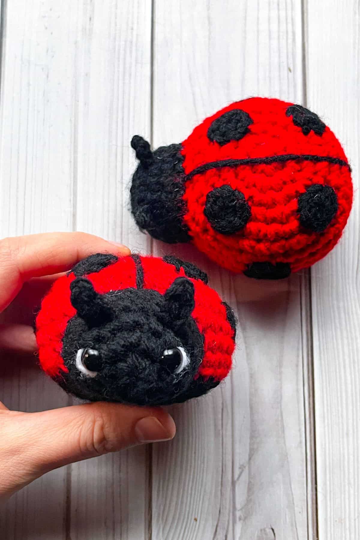 Finished crochet ladybug, one in hand, one on table.