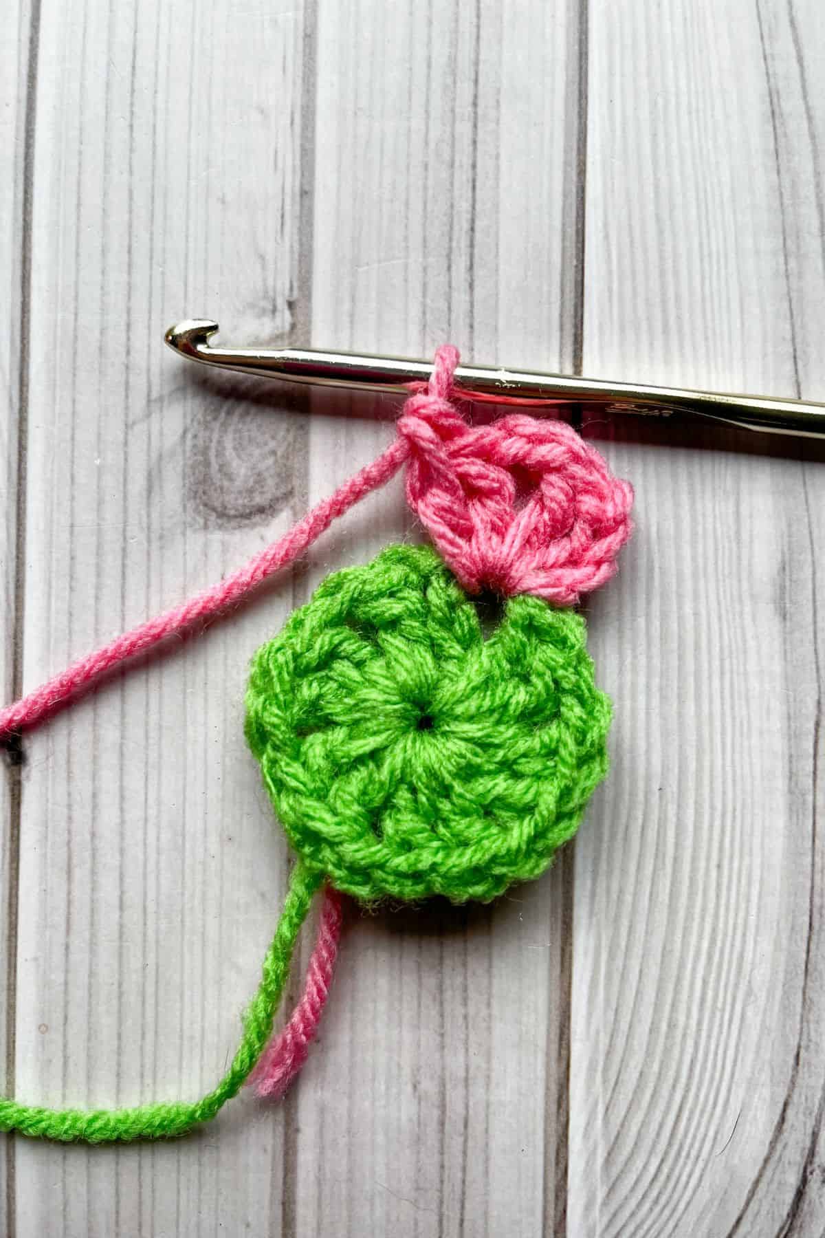 Starting round 2 with pink yarn, lays on table with hook.