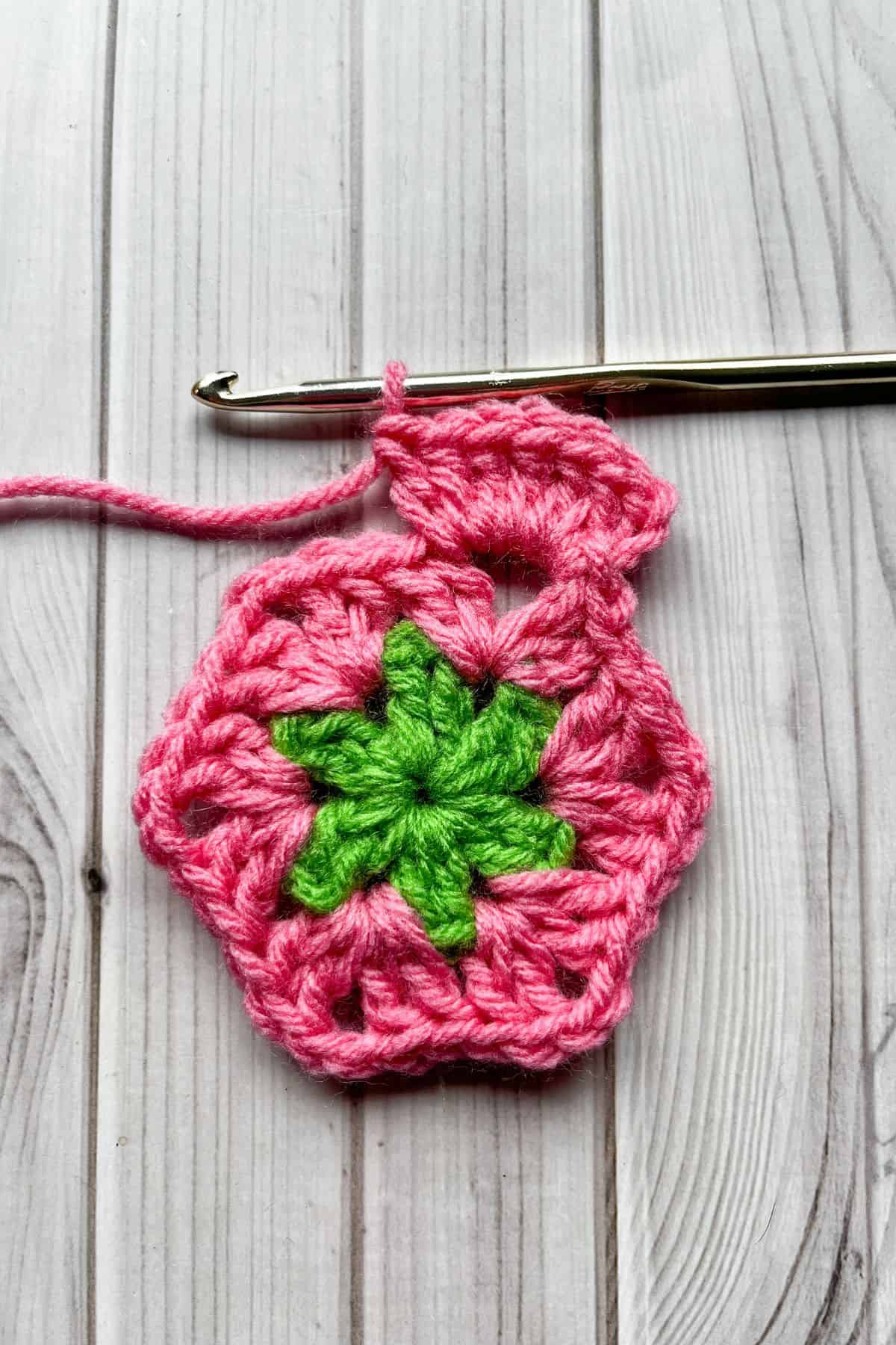 Starting round 3 with pink yarn, and lays on table with hook.