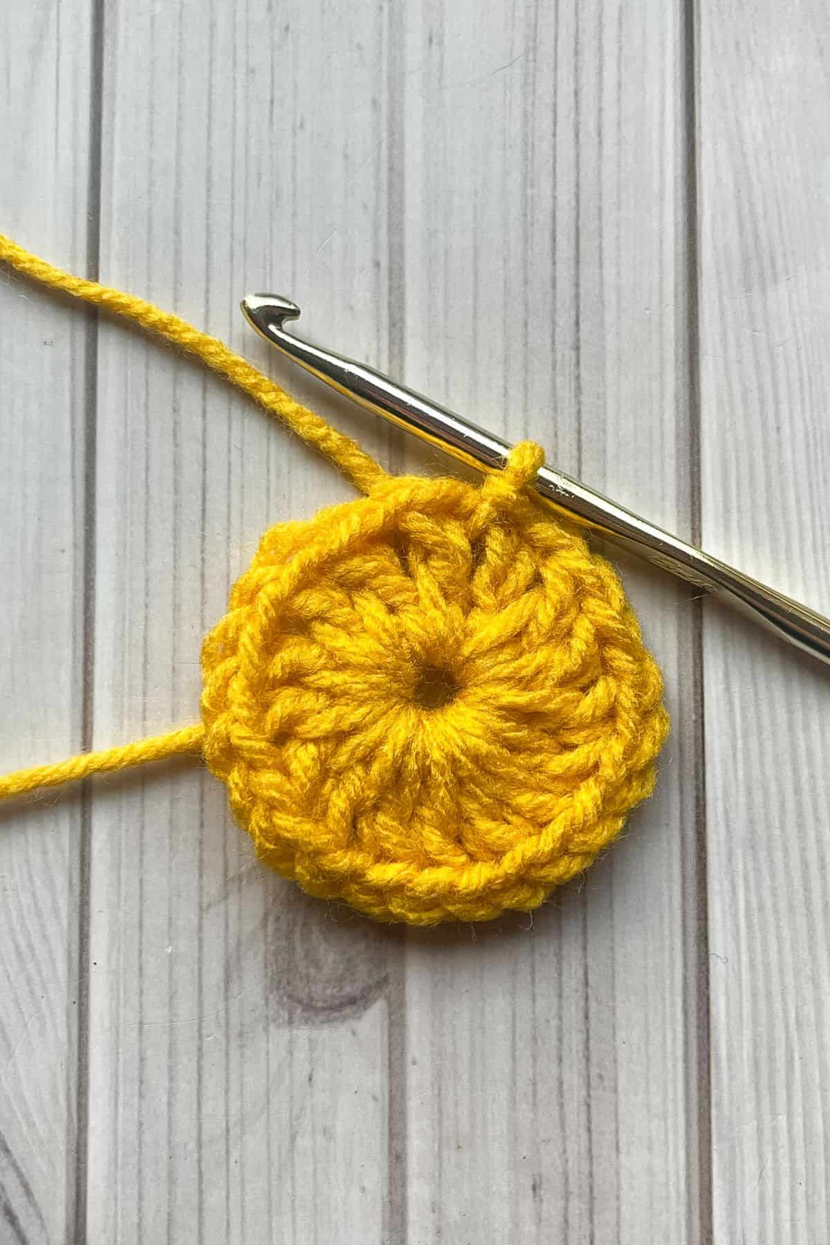Round of yellow double crochet stitches on table with hook.