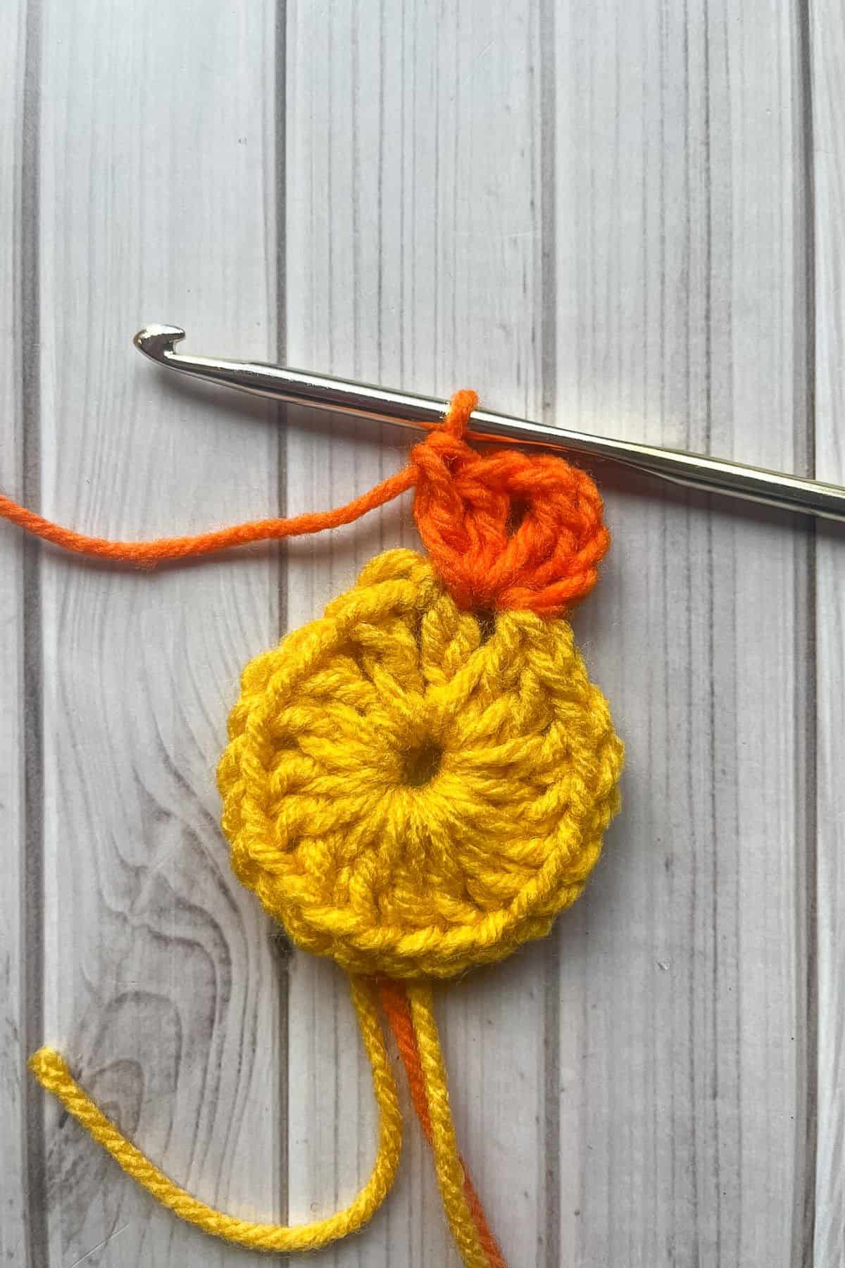 Start of the second round using orange yarn. On table with hook.