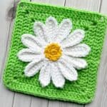 Finished crochet daisy applique on green square on table.