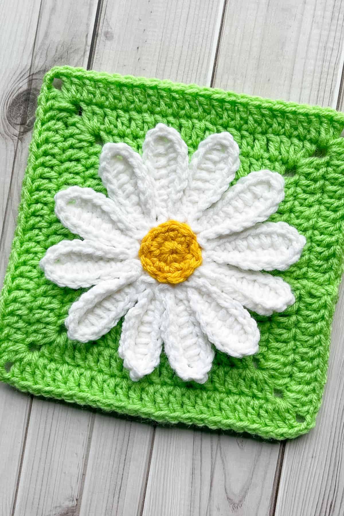 Finished crochet daisy applique on green square on table.