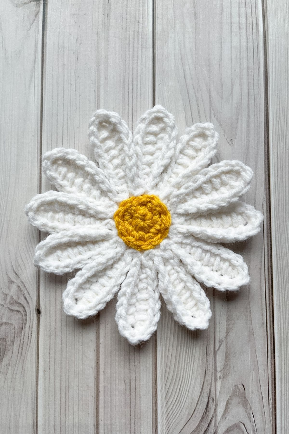 Finished crochet daisy applique laying on a wooden table.