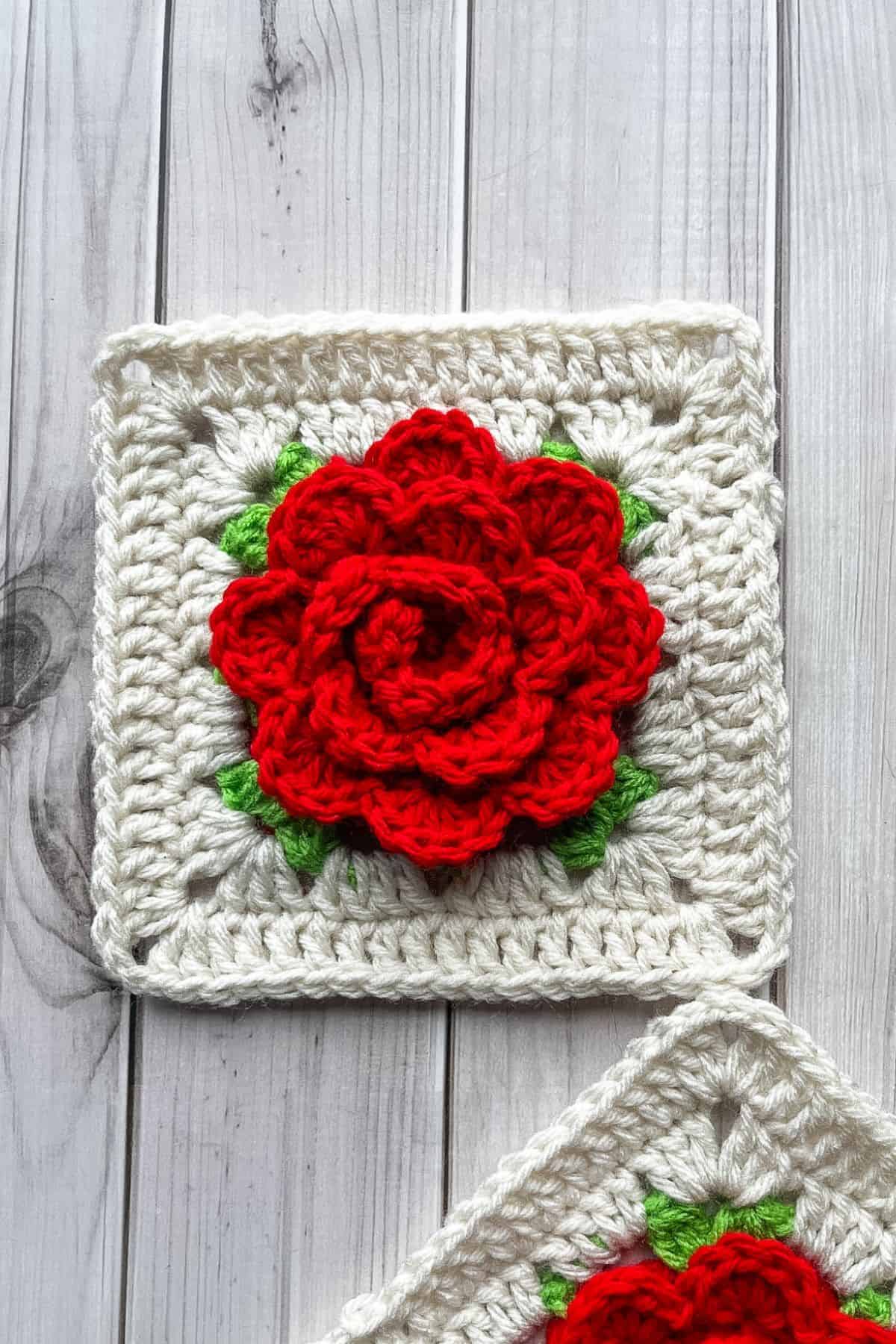 2 finished crochet rose granny squares on a wooden table.