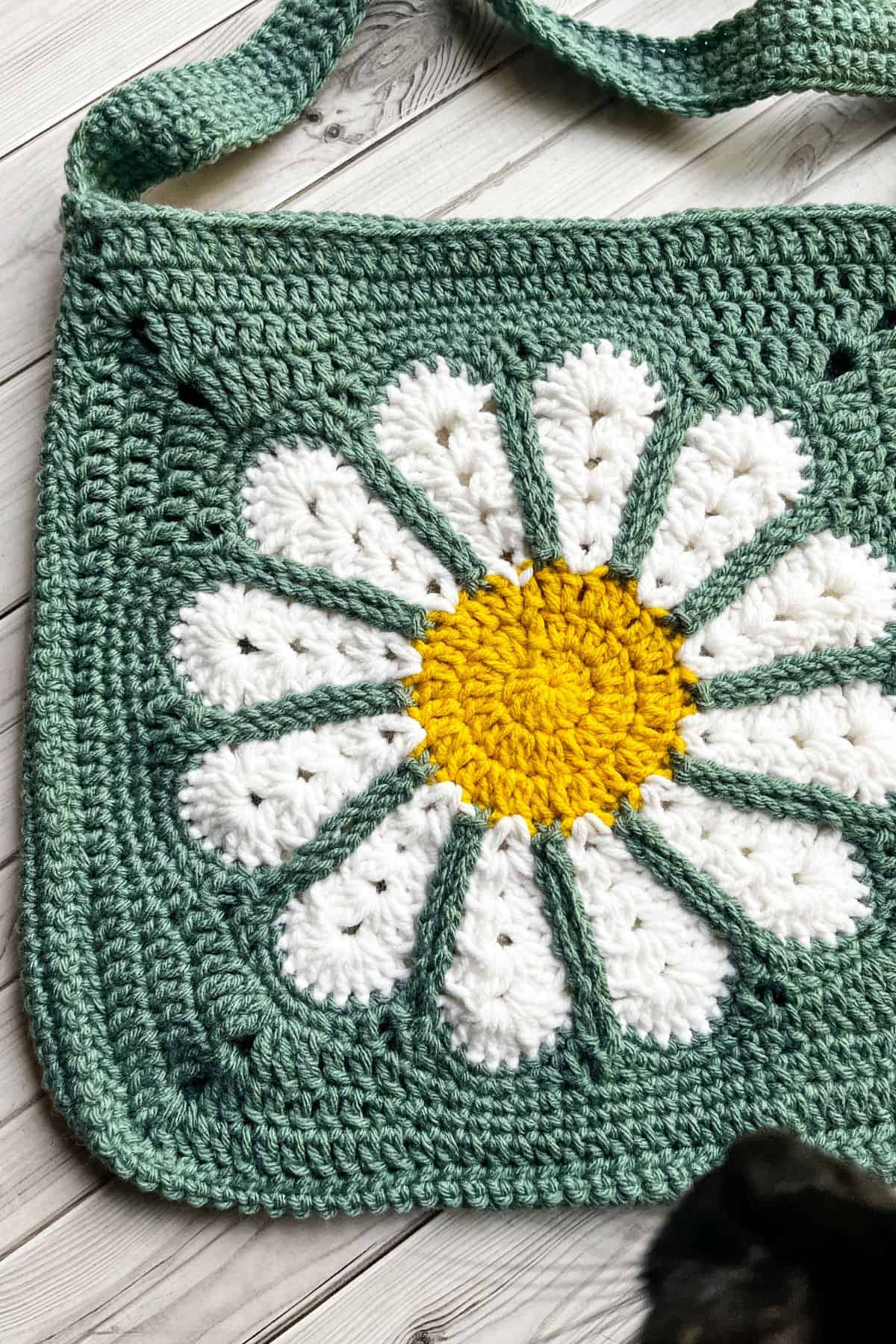 Finished daisy crochet bag pattern on table, with photo bombing cat.