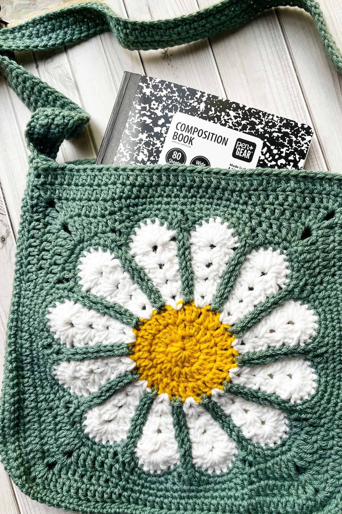 Finished daisy crochet bag pattern on table, with composition notebook in bag.