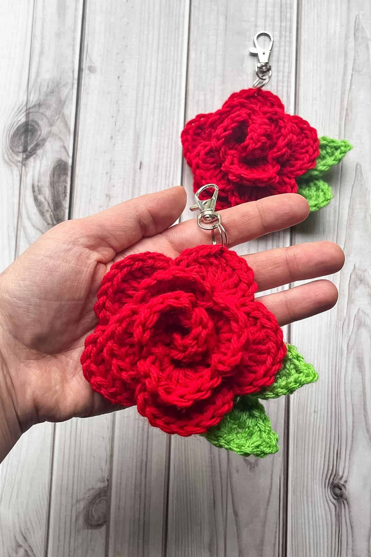 2 finished crochet rose keychains on the table, one in hand.