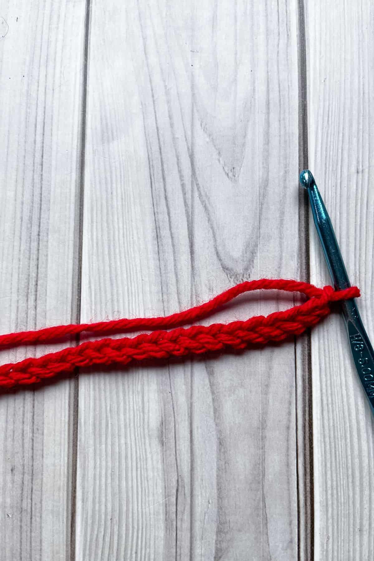 Crochet red chain on the table with a hook.