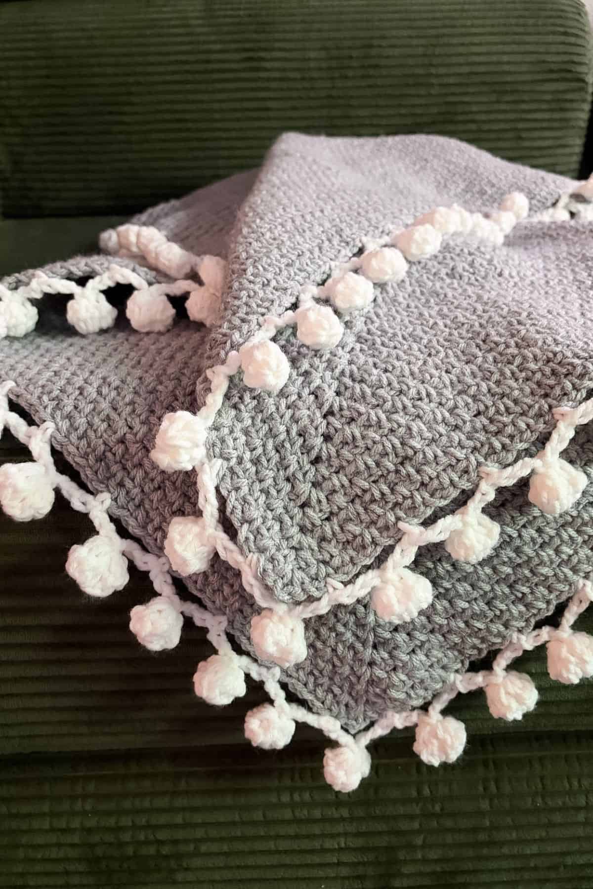 Finished crochet linen stitch blanket with pom pom border on couch.