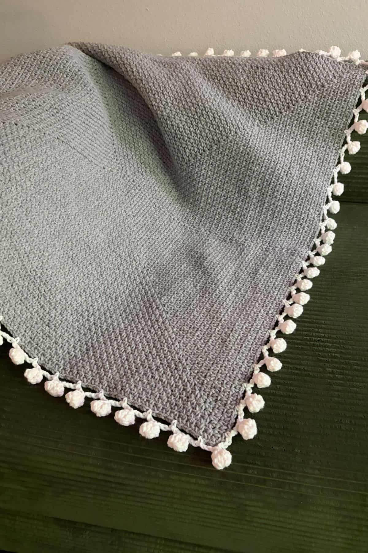 Finished crochet linen stitch blanket with pom pom border on couch.