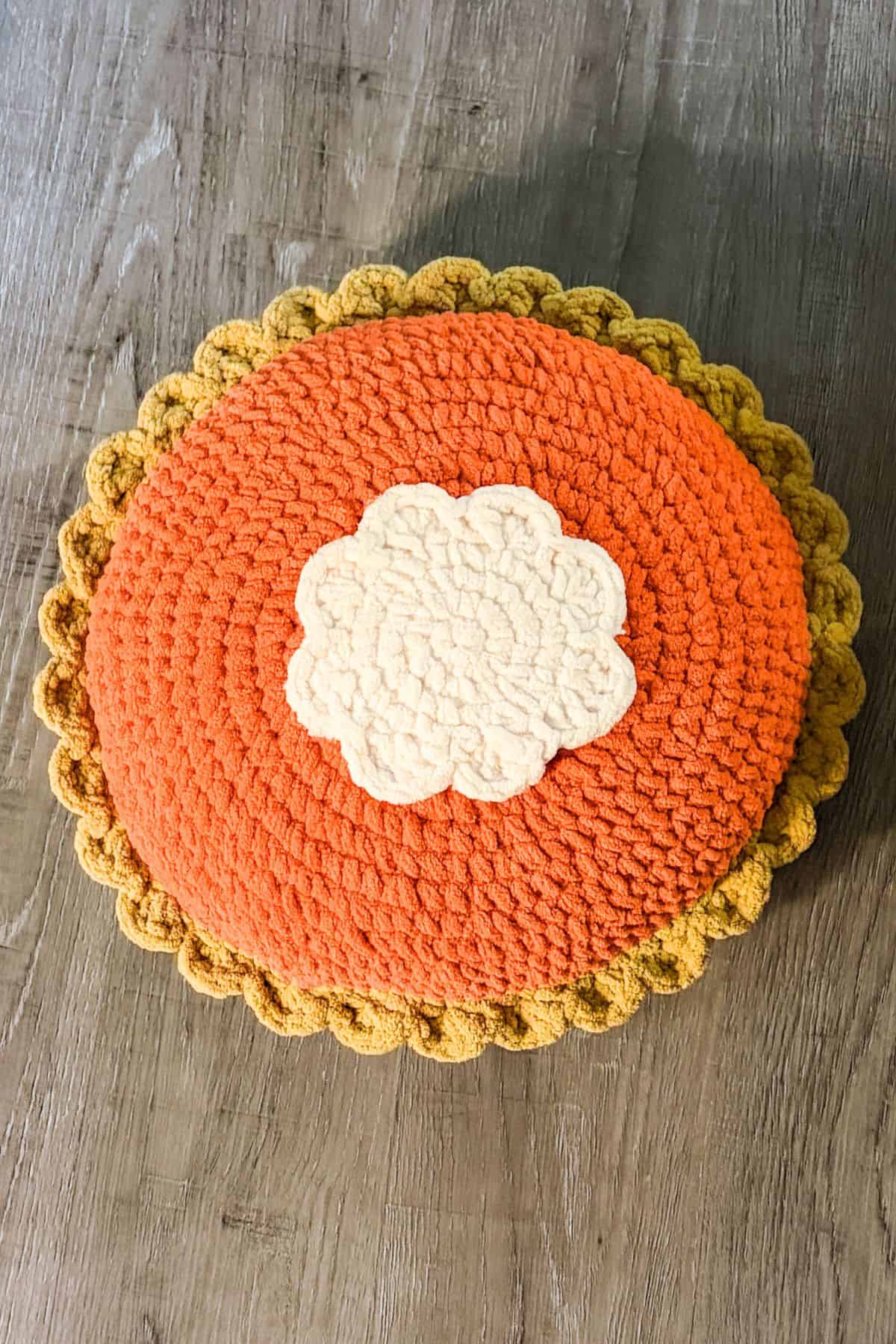 Finished crochet pumpkin pillow on floor.